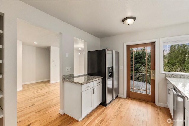 kitchen with light stone counters, white cabinets, appliances with stainless steel finishes, and light hardwood / wood-style floors