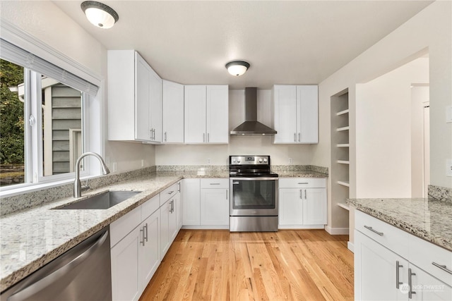 kitchen with appliances with stainless steel finishes, light stone counters, sink, white cabinetry, and wall chimney range hood