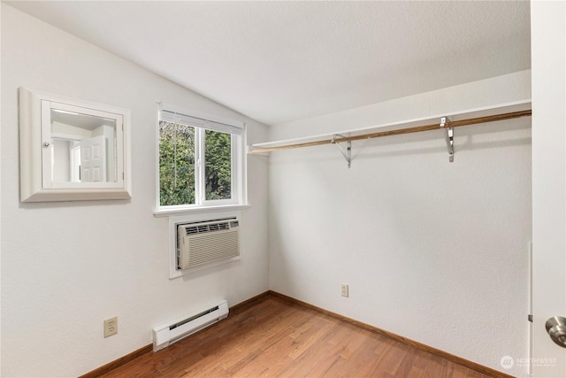 interior space featuring a baseboard radiator, a wall mounted air conditioner, and hardwood / wood-style floors