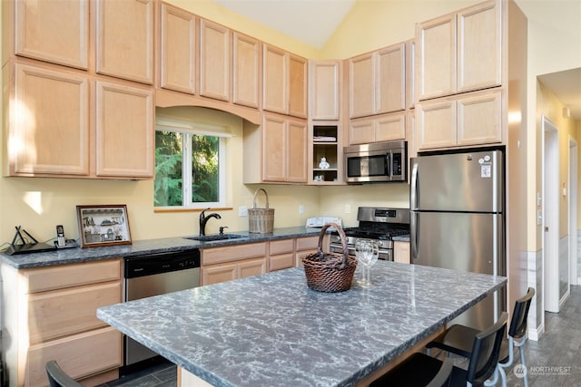 kitchen with lofted ceiling, a kitchen island, stainless steel appliances, dark stone countertops, and light brown cabinetry