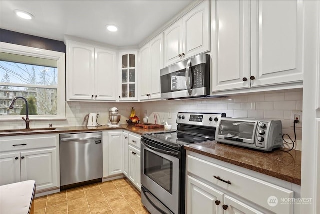 kitchen with a toaster, a sink, white cabinets, appliances with stainless steel finishes, and backsplash