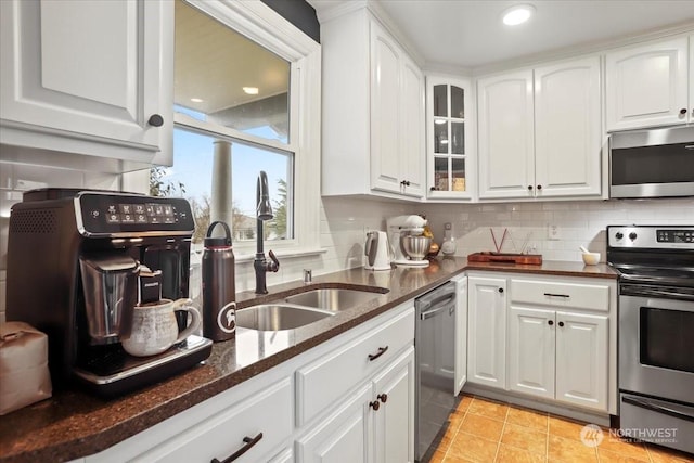 kitchen featuring light tile patterned floors, white cabinetry, appliances with stainless steel finishes, dark stone counters, and sink