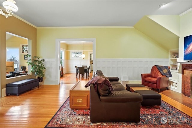 living room with light wood-type flooring, a notable chandelier, a wealth of natural light, and ornamental molding