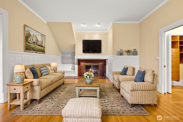 living area with wainscoting, a fireplace with flush hearth, wood finished floors, and crown molding