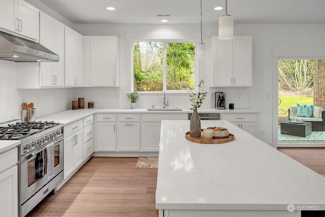 kitchen featuring decorative light fixtures, tasteful backsplash, high end range, sink, and white cabinetry