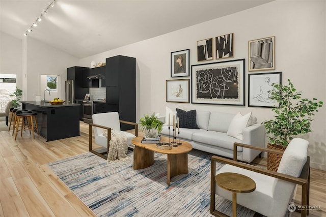 living room featuring light wood-type flooring, track lighting, lofted ceiling, and sink