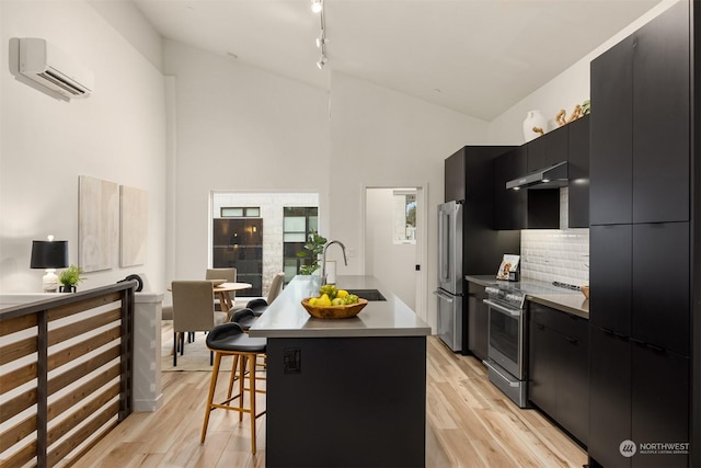 kitchen featuring an island with sink, stainless steel appliances, an AC wall unit, a breakfast bar, and sink