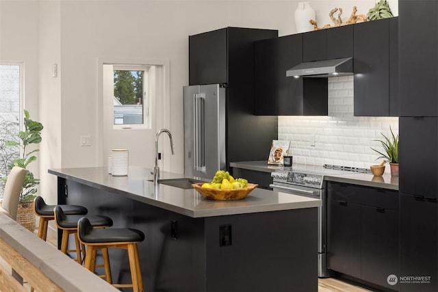 kitchen featuring a kitchen bar, an island with sink, stainless steel appliances, tasteful backsplash, and sink
