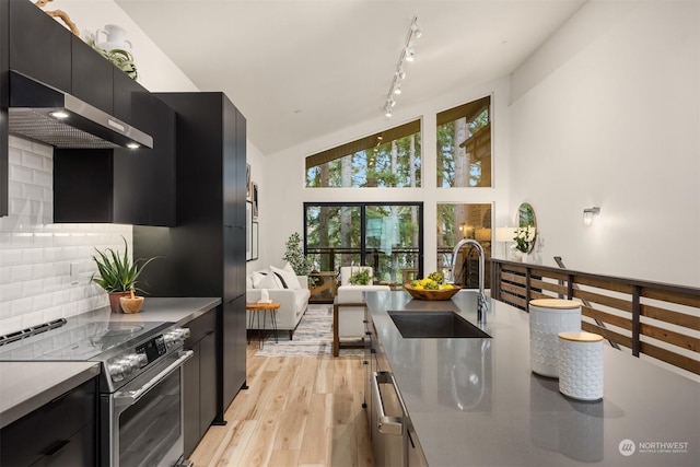 kitchen featuring lofted ceiling, wall chimney exhaust hood, decorative backsplash, sink, and stainless steel electric range oven