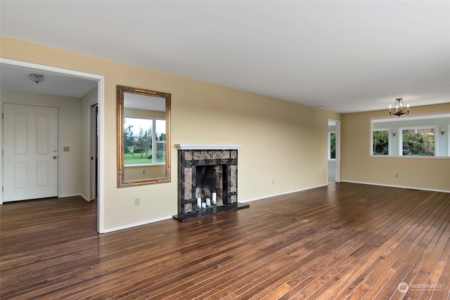 unfurnished living room with dark wood-type flooring, plenty of natural light, a premium fireplace, and a notable chandelier