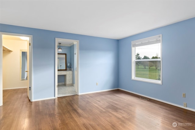 unfurnished bedroom with hardwood / wood-style flooring, a walk in closet, and ensuite bathroom