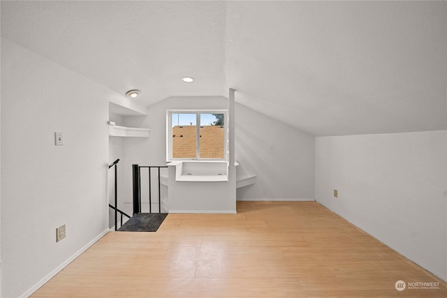 additional living space featuring vaulted ceiling, a textured ceiling, and light hardwood / wood-style flooring