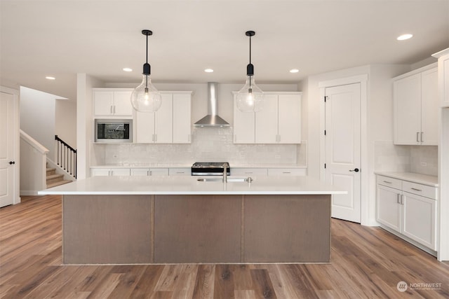 kitchen featuring wall chimney exhaust hood, a center island with sink, white cabinets, and wood-type flooring