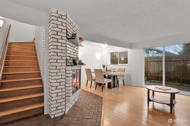 dining area with a brick fireplace, a textured ceiling, and hardwood / wood-style floors