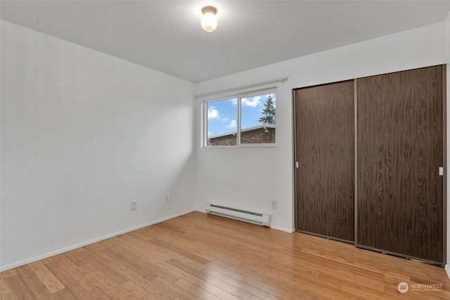 unfurnished bedroom featuring light hardwood / wood-style floors, baseboard heating, and a closet