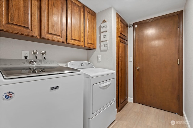 laundry area featuring washing machine and dryer, cabinets, and light hardwood / wood-style flooring