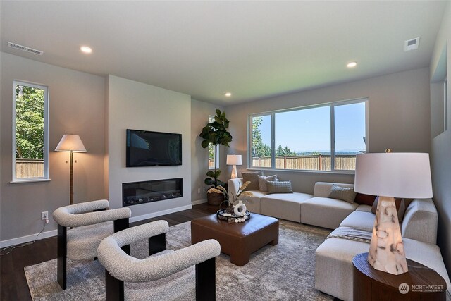 living area featuring dark wood-type flooring, plenty of natural light, a glass covered fireplace, and visible vents