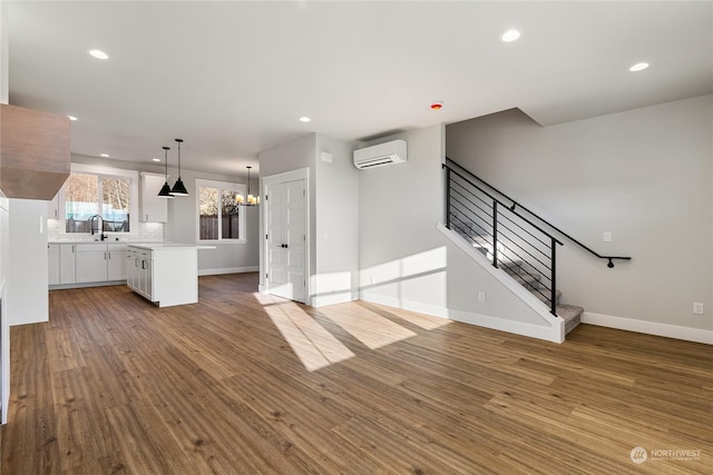 unfurnished living room featuring wood-type flooring, sink, a wall mounted air conditioner, and a chandelier