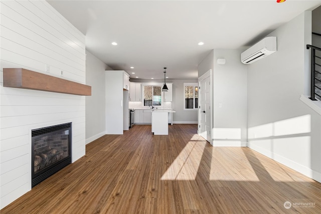 unfurnished living room with dark wood-type flooring, a large fireplace, and an AC wall unit