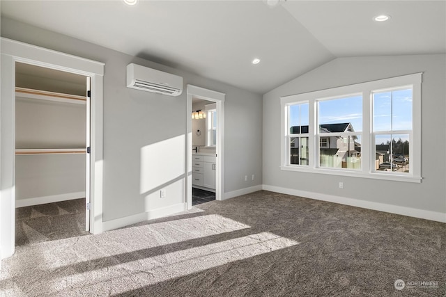 unfurnished bedroom featuring lofted ceiling, connected bathroom, a wall mounted AC, and dark carpet