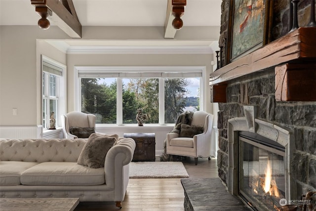 living room with a healthy amount of sunlight, beam ceiling, wood-type flooring, and a stone fireplace