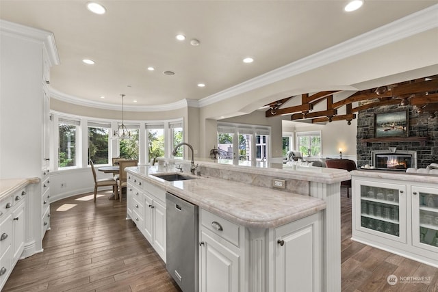 kitchen with dishwasher, white cabinetry, a stone fireplace, an island with sink, and sink