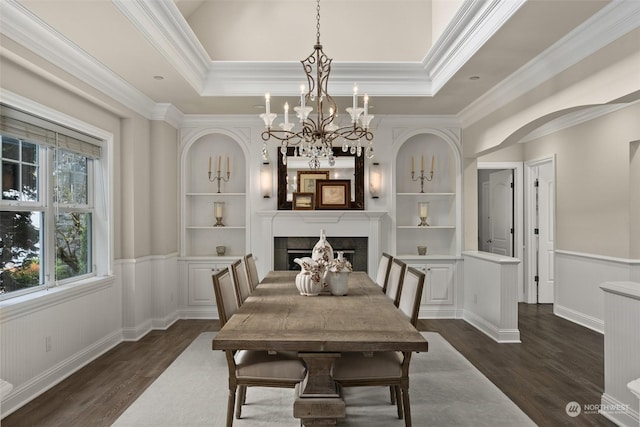 dining area with a fireplace, a raised ceiling, built in features, dark wood-type flooring, and ornamental molding