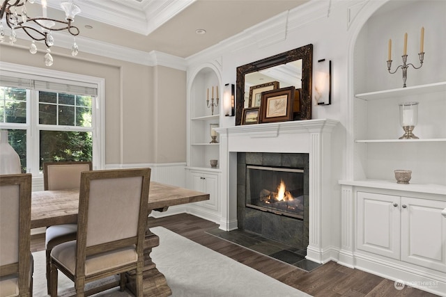 dining area featuring built in shelves, dark hardwood / wood-style flooring, an inviting chandelier, crown molding, and a tiled fireplace