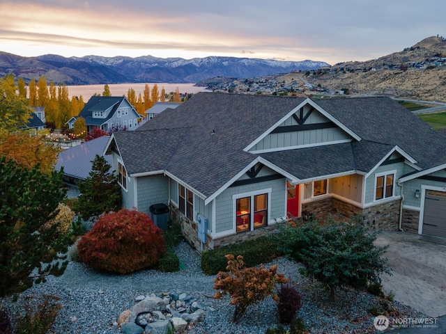 craftsman-style house with a mountain view, stone siding, roof with shingles, and driveway