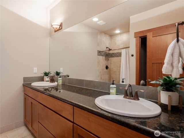 full bath with a tile shower, tile patterned flooring, double vanity, and a sink