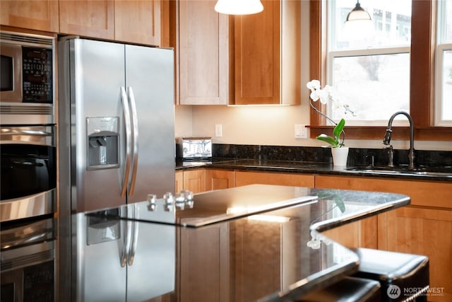 kitchen with hanging light fixtures, brown cabinets, stainless steel appliances, and a sink