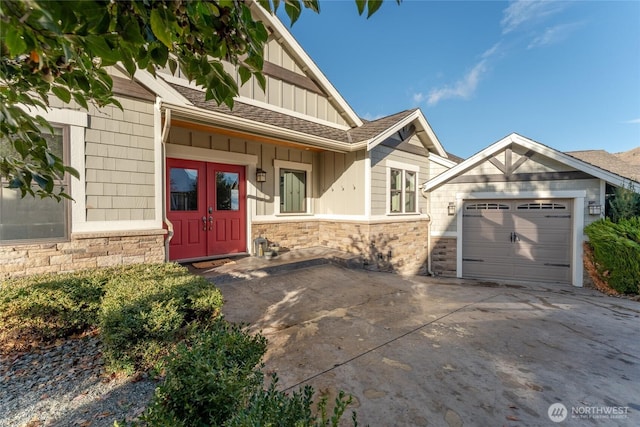 entrance to property with driveway, roof with shingles, a garage, stone siding, and board and batten siding