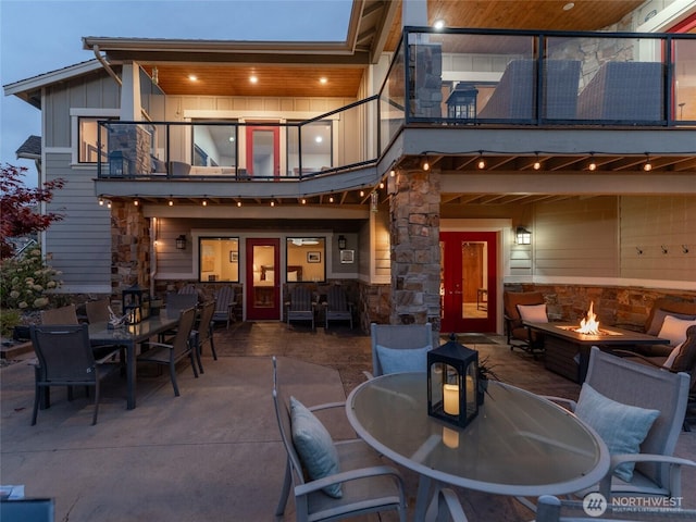 back of property with outdoor dining space, a balcony, board and batten siding, and a patio