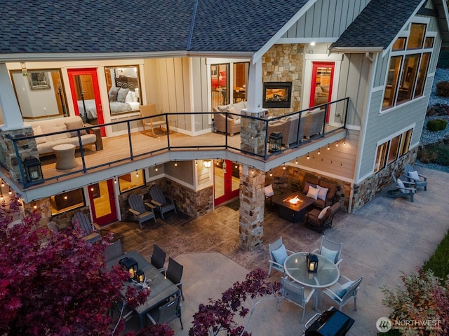 exterior space with board and batten siding, a shingled roof, outdoor dining area, stone siding, and a patio