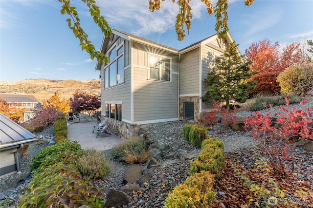 view of home's exterior with board and batten siding, a mountain view, a patio area, and stone siding