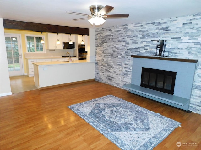 living room with sink, ceiling fan, light hardwood / wood-style floors, and a large fireplace