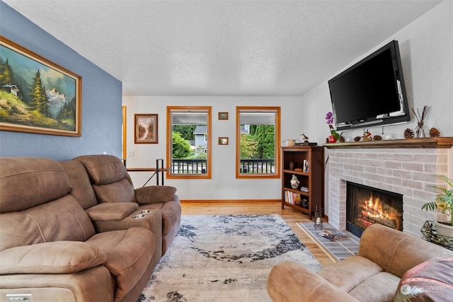 living room with a textured ceiling, a brick fireplace, and light hardwood / wood-style flooring