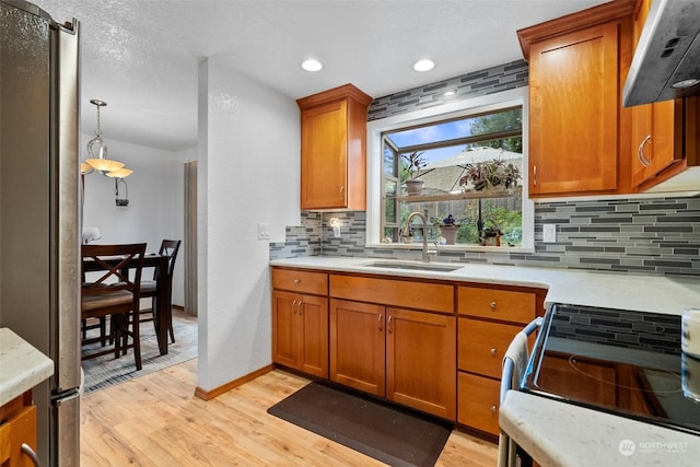 kitchen featuring stainless steel appliances, range hood, pendant lighting, light hardwood / wood-style flooring, and sink