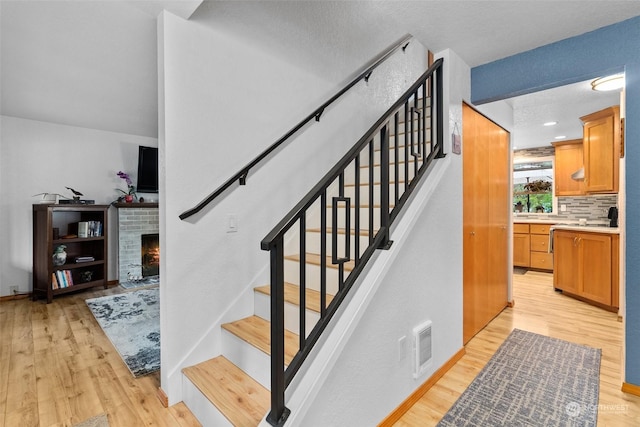 staircase featuring a textured ceiling, a brick fireplace, and hardwood / wood-style flooring