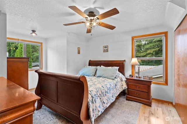 bedroom with a textured ceiling, ceiling fan, light hardwood / wood-style floors, and multiple windows