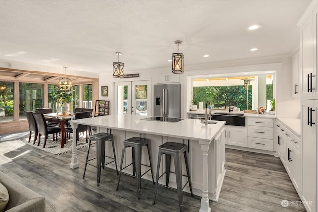 kitchen with decorative light fixtures, high end refrigerator, an island with sink, white cabinets, and french doors