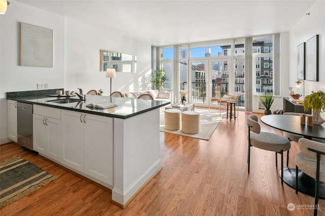 kitchen featuring dishwasher, sink, white cabinets, expansive windows, and kitchen peninsula