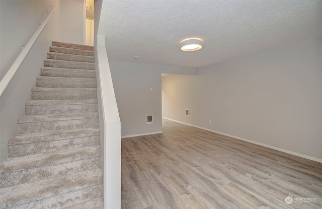 stairs with a textured ceiling and wood-type flooring