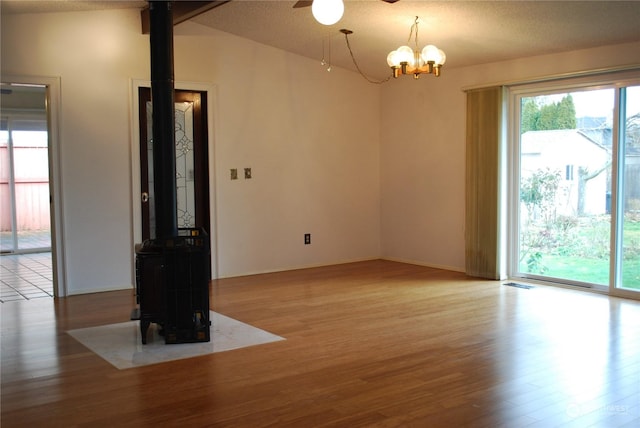 spare room featuring light wood-type flooring, vaulted ceiling, a healthy amount of sunlight, and a wood stove