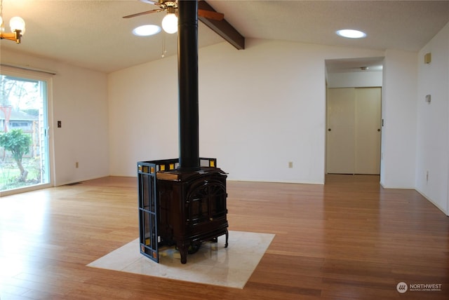 living room with hardwood / wood-style floors, vaulted ceiling with beams, ceiling fan, and a wood stove