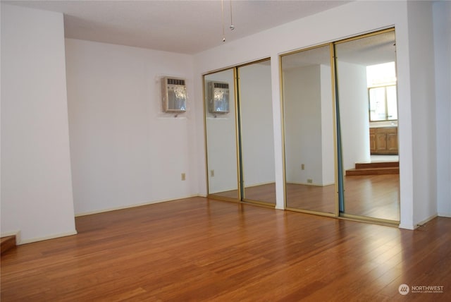 unfurnished bedroom with a wall mounted air conditioner, hardwood / wood-style flooring, and multiple closets