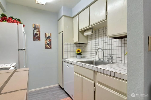 kitchen with dishwasher, white fridge, tasteful backsplash, sink, and light wood-type flooring