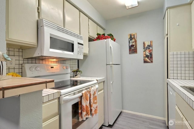 kitchen with decorative backsplash, white appliances, light hardwood / wood-style flooring, tile counters, and cream cabinetry