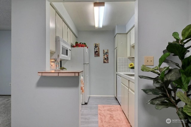 kitchen featuring light wood-type flooring, decorative backsplash, and white appliances