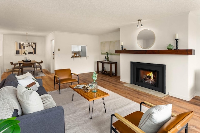 living room featuring a textured ceiling, ornamental molding, an inviting chandelier, and light wood-type flooring